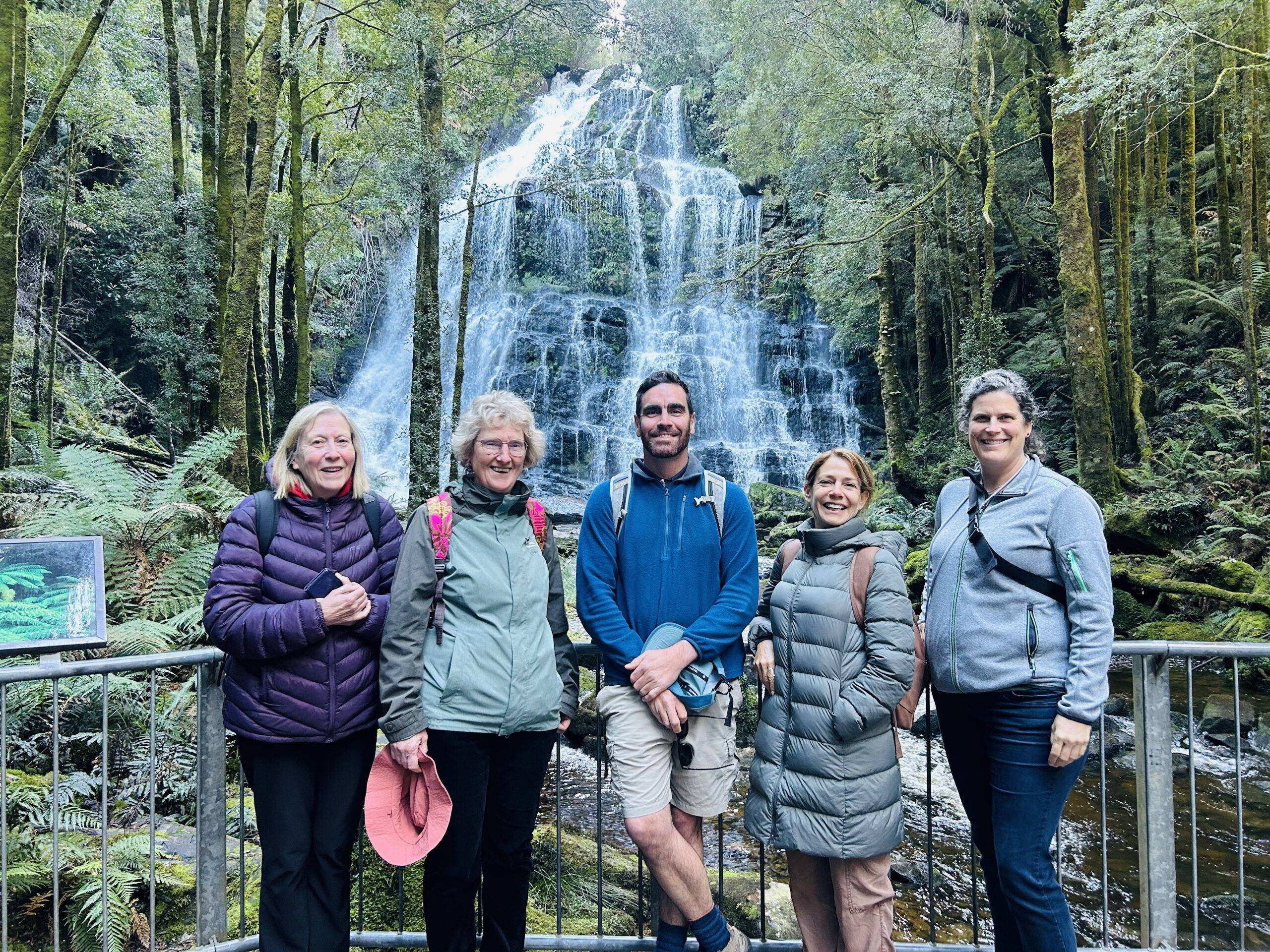 Four ladies stand with their male tour guide at centre in front of a beautiful cascading waterfall called Nelson Falls